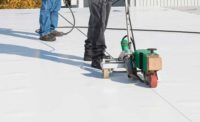 Work boots belonging to 2 roofing professionals are visible as sealant is applied to a commercial roof