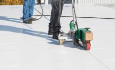 Work boots belonging to 2 roofing professionals are visible as sealant is applied to a commercial roof